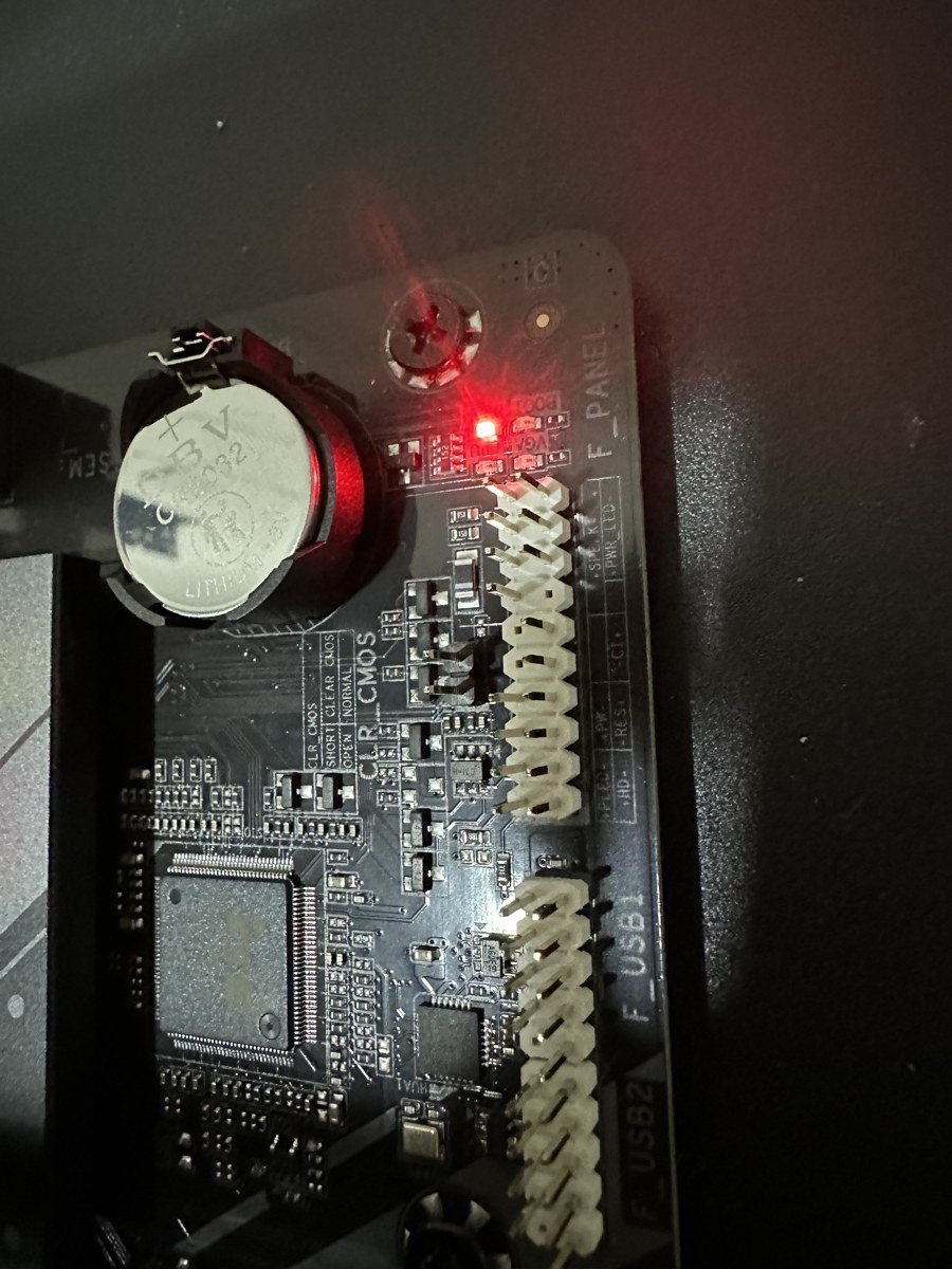 Close-up of the motherboard's status LEDs with the DRAM debug LED lit red beside the CMOS battery and front-panel headers.